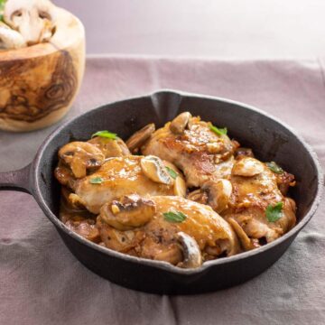 A cast iron pan with chicken mushroom an garlic in a yummy sauce.