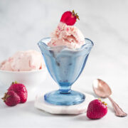 A clear blue colored dessert glass filled with strawberry ice cream and a fresh strawberry garnish on top.