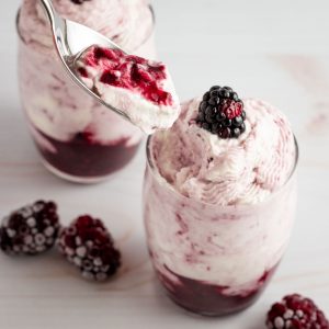 Two blackberry cream desserts with a spoon coming out of one. out