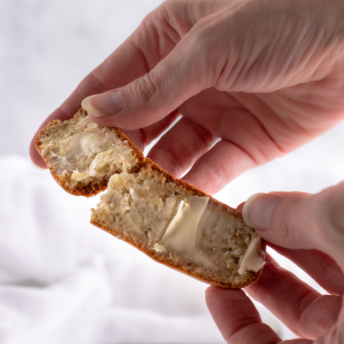 Two hands holding and breaking apart a slice of buttered bread.