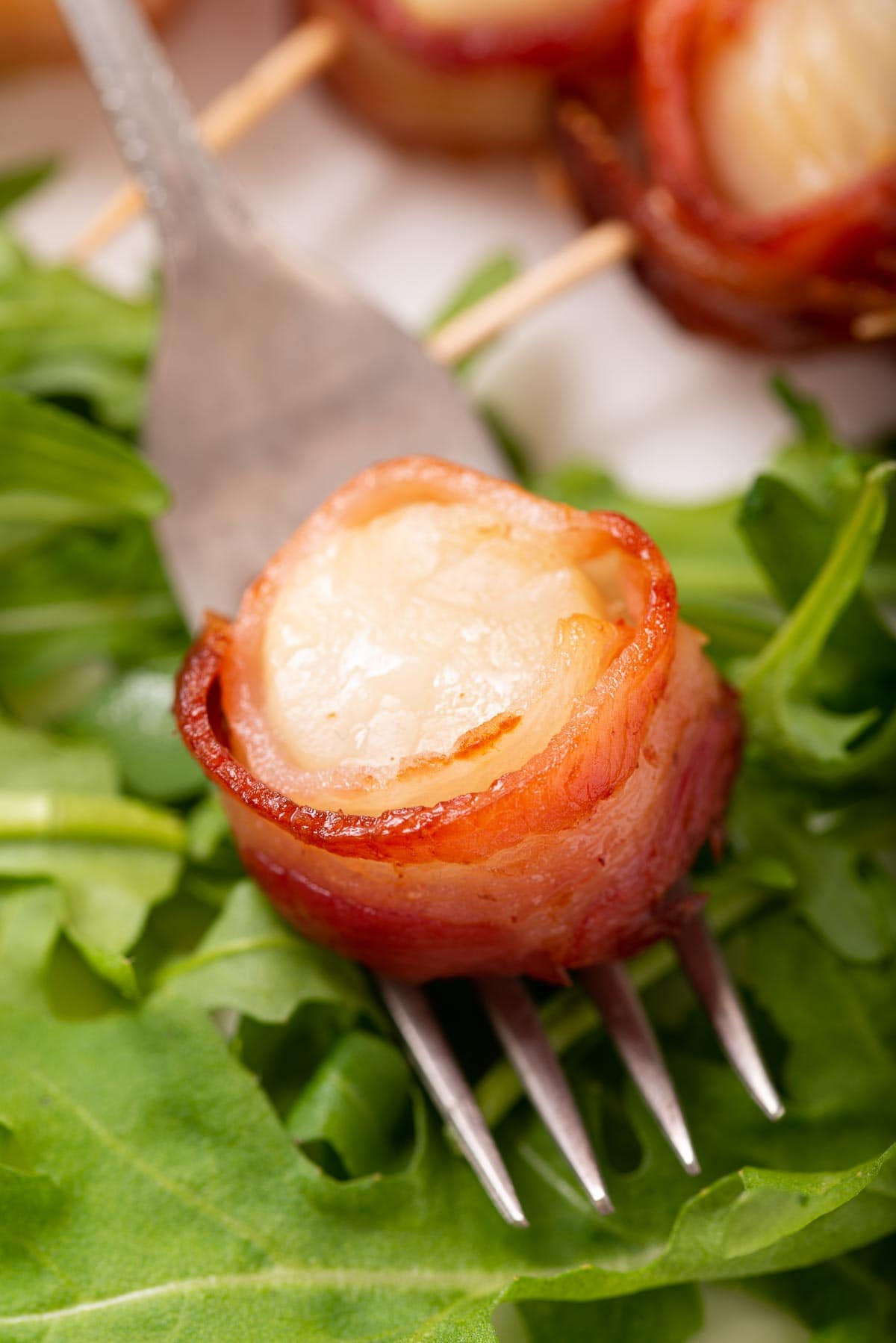 A fork with a bacon wrapped scallop on it.