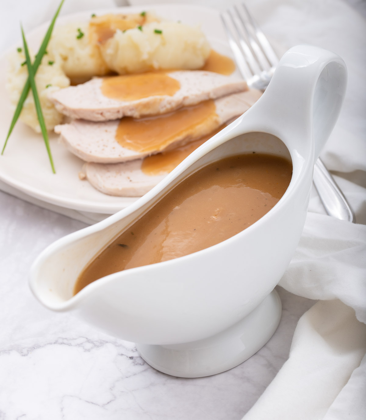 A gravy boat filled with turkey gravy and roast turkey breast and mashed cauliflower  in the background.