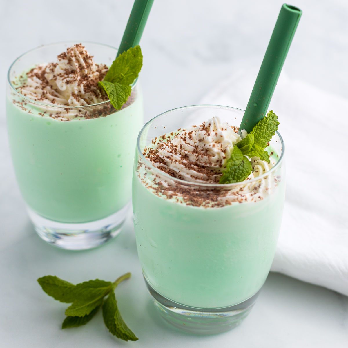 Two keto shamrock milkshakes with whipped cream and shave chocolate and fresh mint leaves.