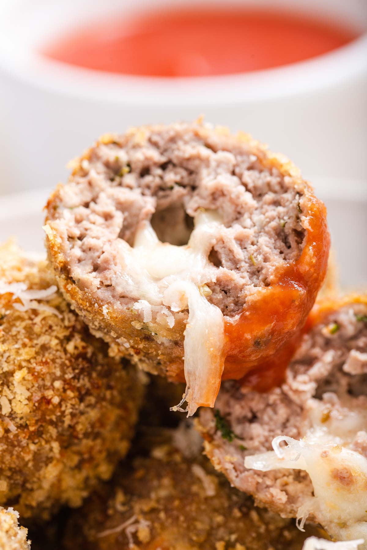 A stack of keto cheese stuffed air fryer meatballs with one meatball cut in half and cheese oozing out.